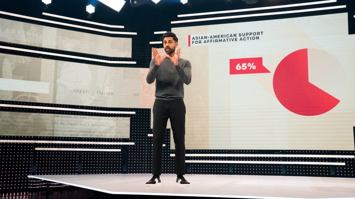 Hasan Minhaj dengan sweater abu-abu di Patriot Act menjelaskan sebuah diagram
